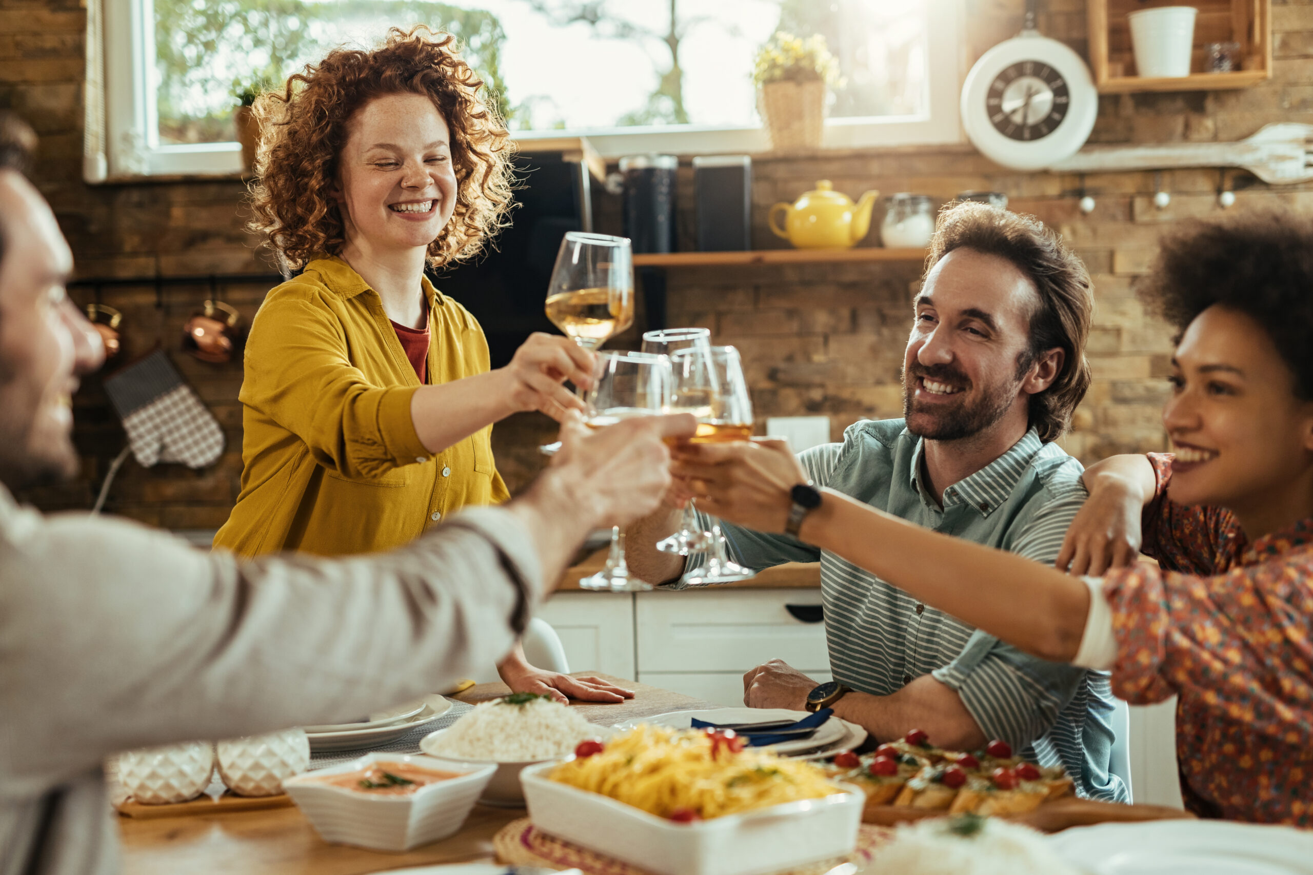 A joyful group of friends raising glasses in a toast at a dinner gathering, surrounded by delicious food.